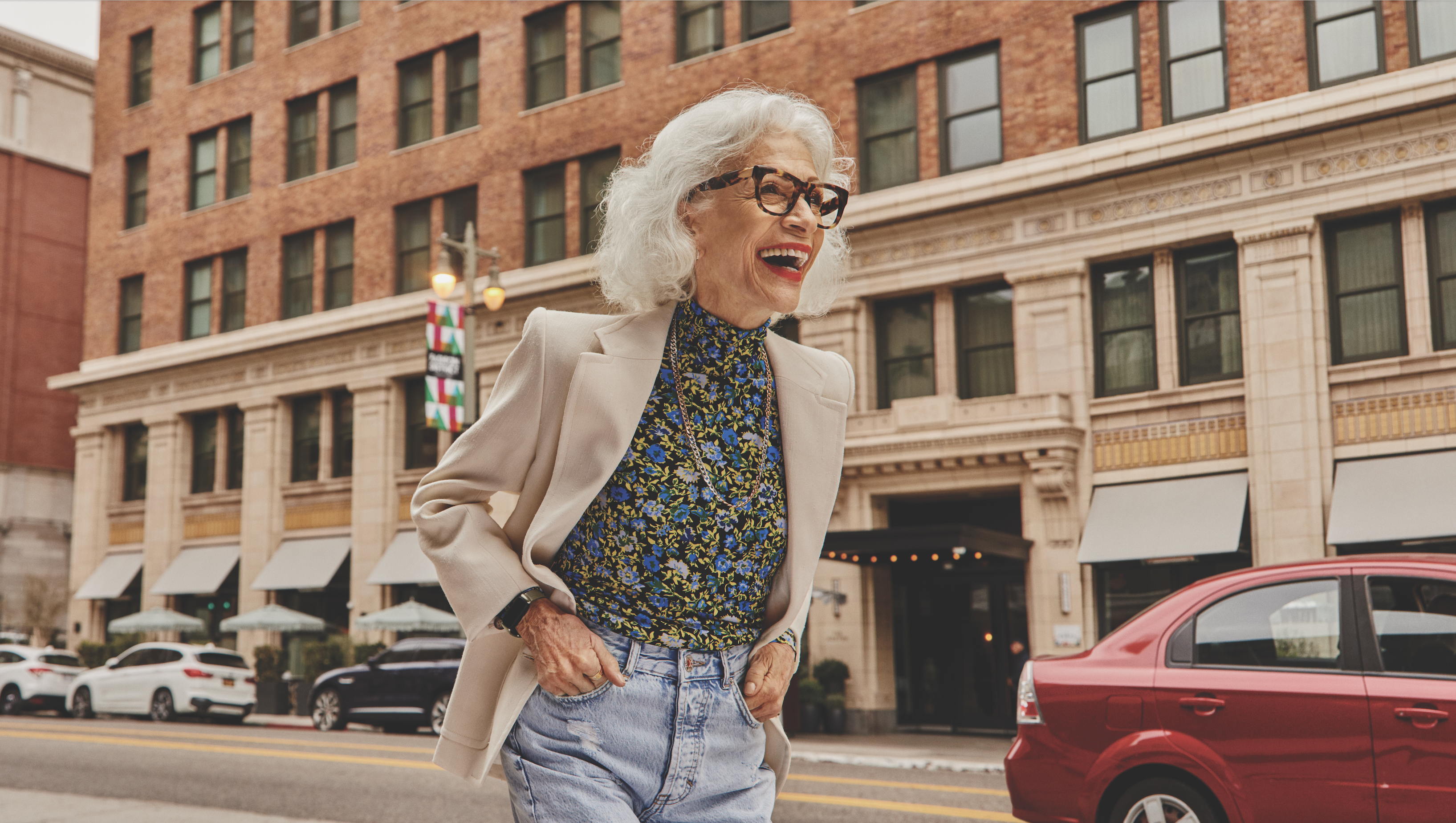 Older woman laughing with hands in her pocket walking down a street