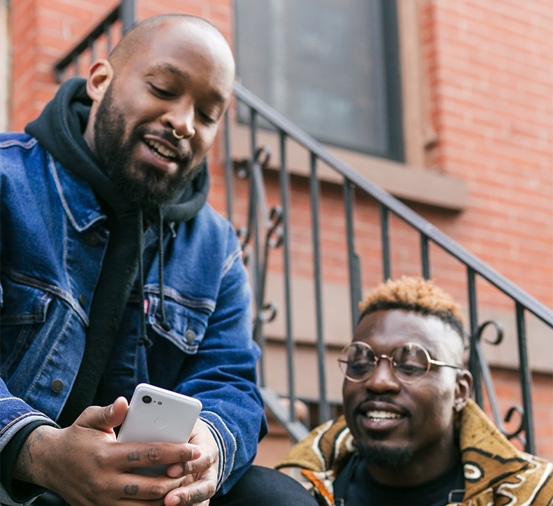 two black people sitting on steps looking at phone